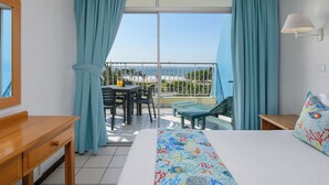 Een hotelkamer met een balkon, een bed met een kleurrijk beddegoed, een houten nachtkastje en een tafel met stoelen buiten.