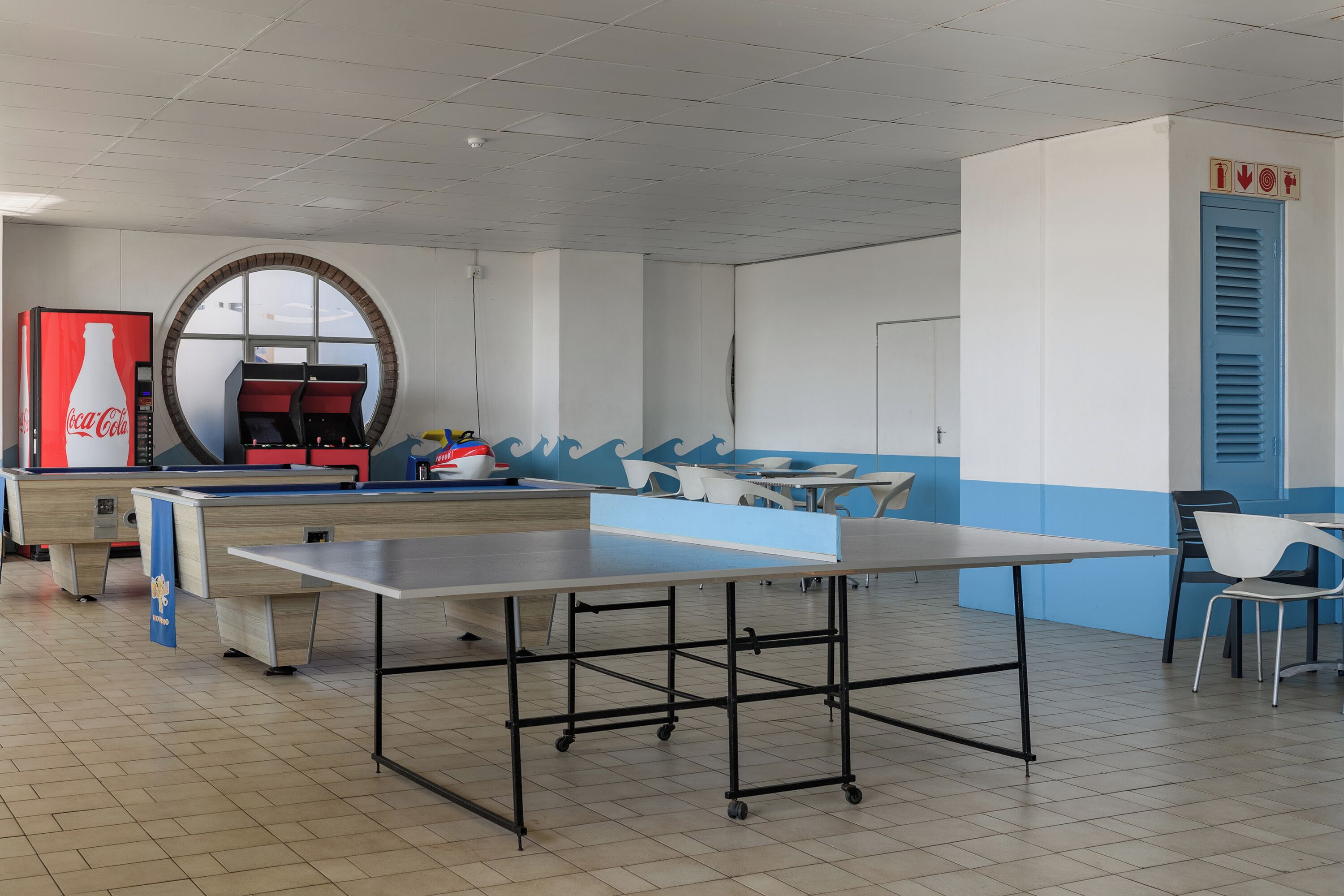 Een ruime kamer met een tafeltennistafel, een Coca-Cola koelkast en een blauw-wit kleurenschema.