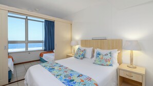 Een hotelkamer met een groot bed, twee nachtkastjes, een raam met uitzicht op zee en een deur naar een balkon.