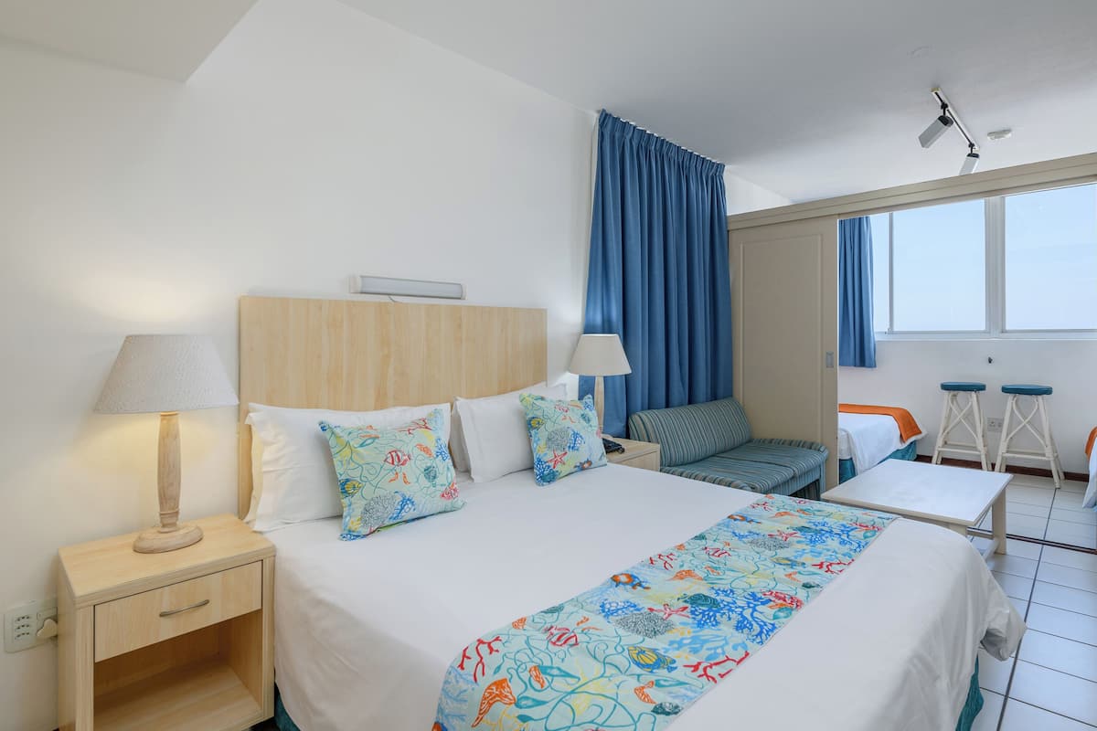 A hotel room with a bed, two bedside tables, a nightstand, a sofa, a small table, and a window with curtains.