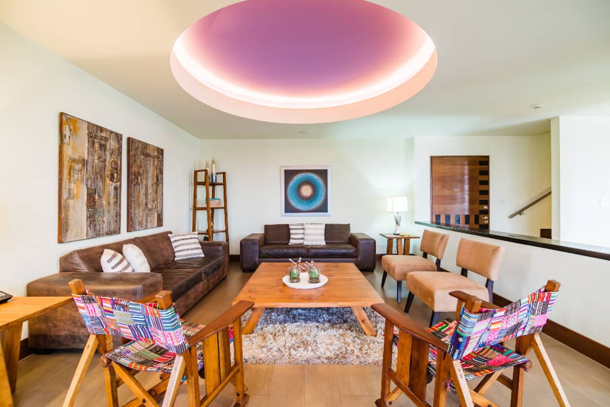 Ein modernes Wohnzimmer mit Couchtisch aus Holz, zwei Sofas, bunten Sesseln und abstrakter Wandkunst.
