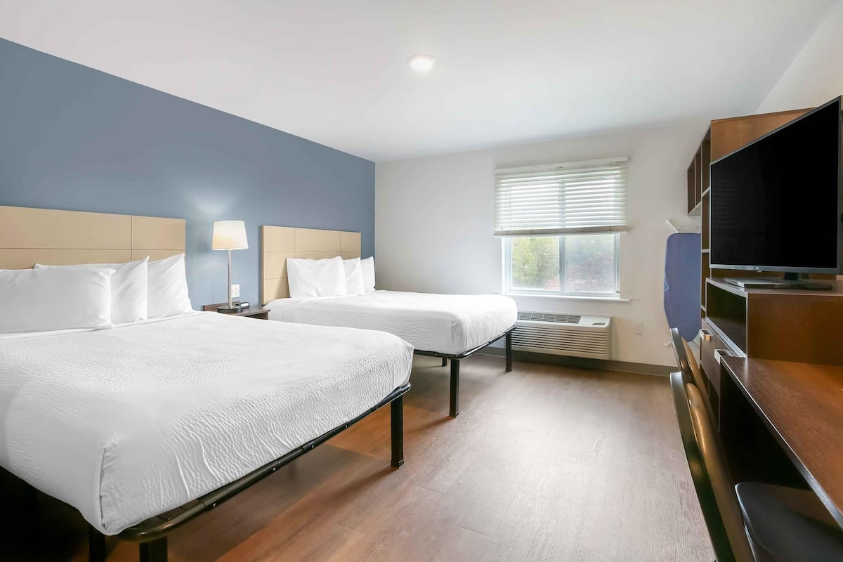A hotel room with two beds, a TV, and a window with blinds.