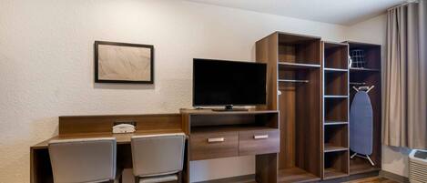 A hotel room with a wooden desk, two chairs, a flat-screen TV, a coat rack, and a wardrobe.