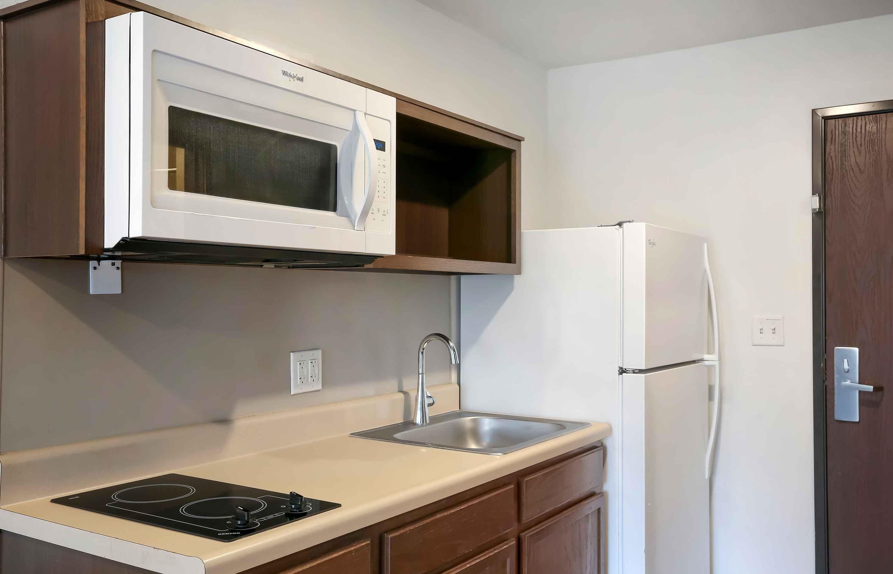 Cocina compacta con microondas integrado, pileta de acero inoxidable y refrigerador blanco.