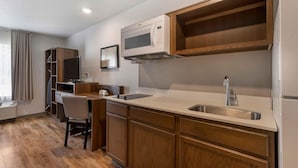 A compact kitchen with a microwave, sink, and wooden cabinets. - Extended Stay America Select Suites Tampa Brandon East (Tampa)