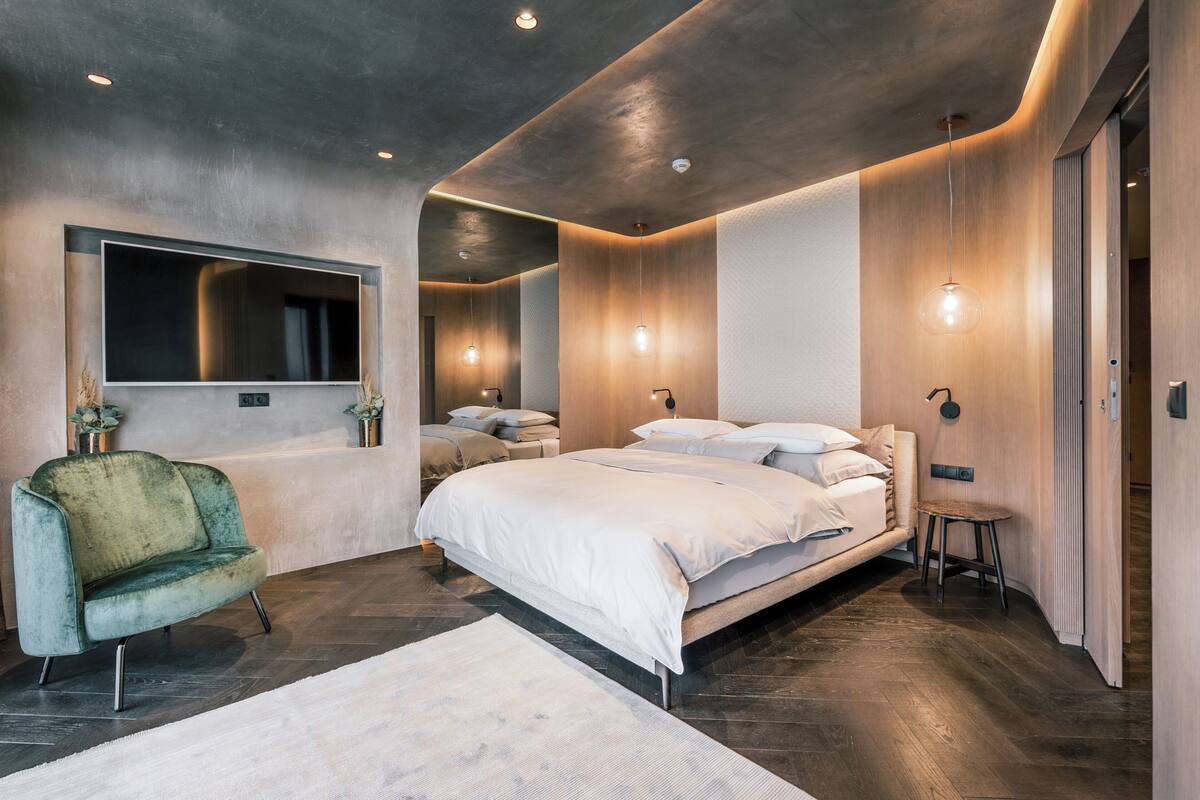 Une chambre moderne avec un grand lit, une coiffeuse avec un miroir et un fauteuil vert.