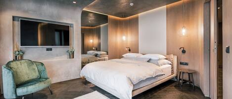 A modern bedroom with a large bed, a vanity with a mirror, and a green armchair.