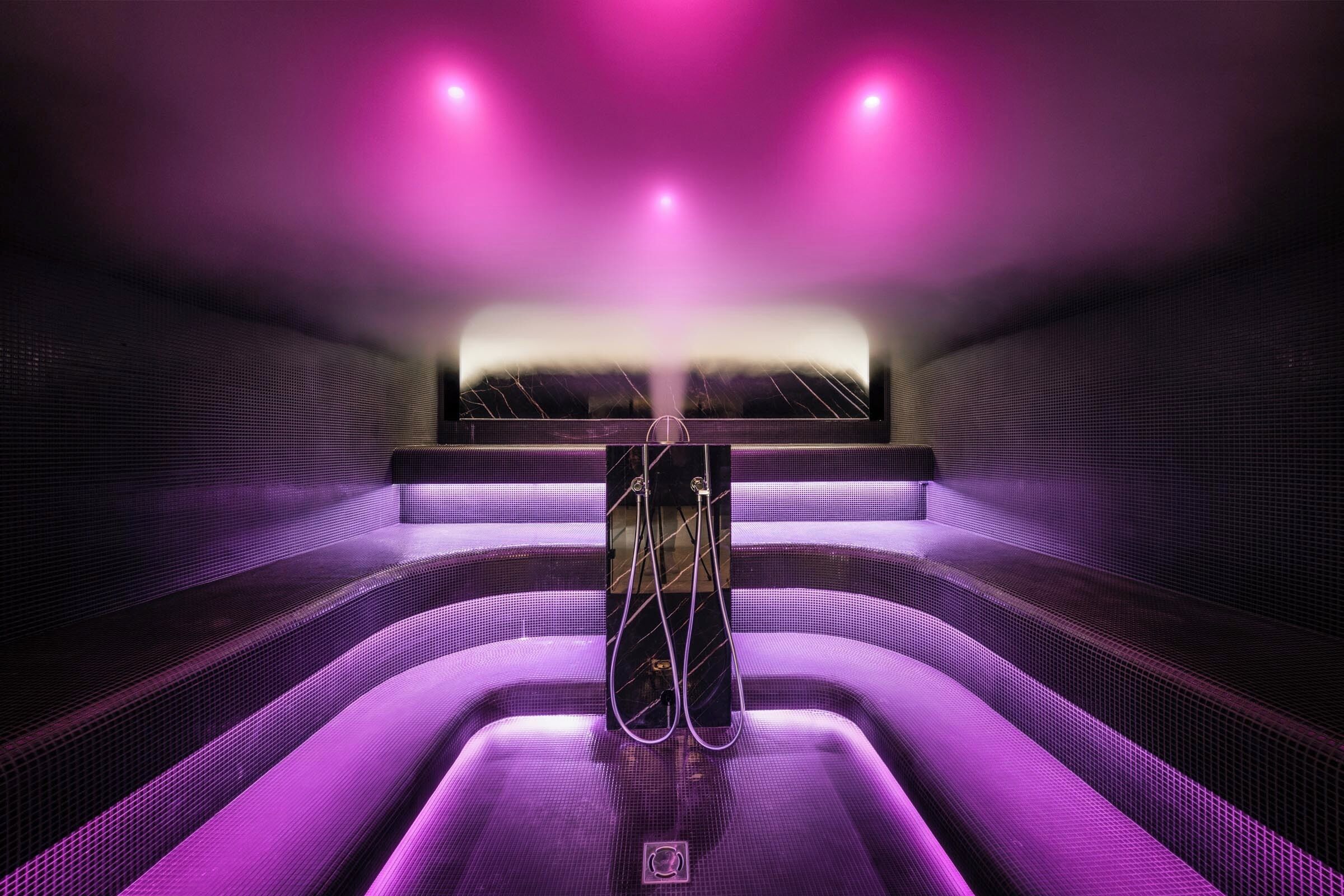 Een modern wellnesscentrum met een centraal gelegen jacuzzi, omringd door treden en verlicht met paars licht.