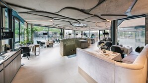 A modern interior with a curved ceiling, a reception desk, and dining area with tables and chairs. - Quellenhof See Lodge (San Martino in Passiria)