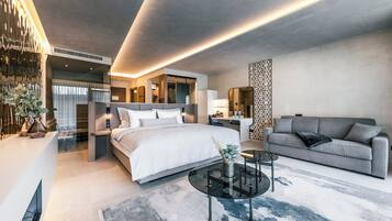 Una habitación de hotel moderna con una cama grande, un sofá gris, una mesa de centro de cristal y un panel decorativo en la pared.