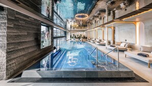 A modern indoor pool with a glass ceiling, stone walls, and contemporary furnishings. - Quellenhof See Lodge (San Martino in Passiria)