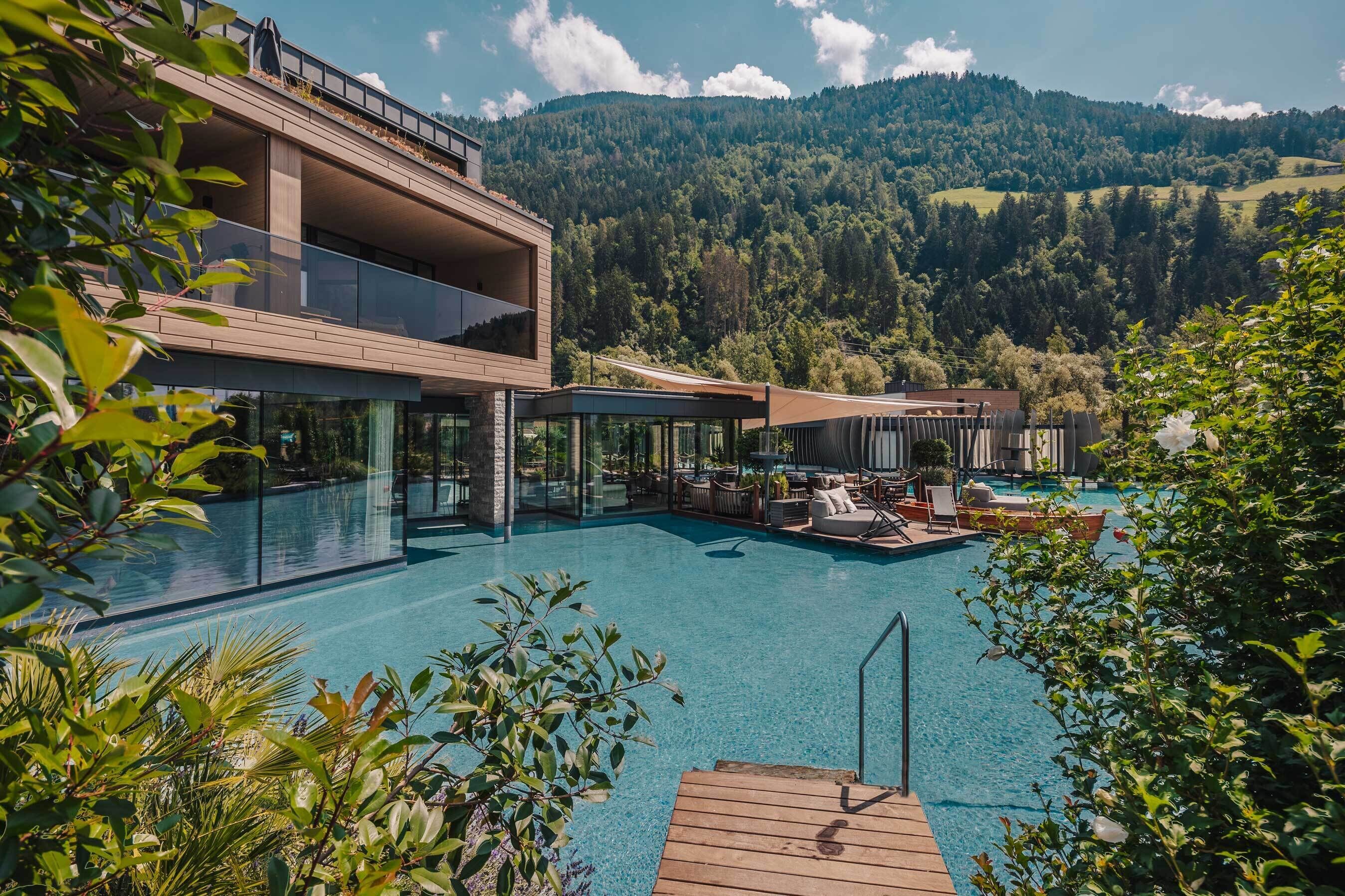 A modern resort with a large pool, outdoor seating, and a view of the mountains.