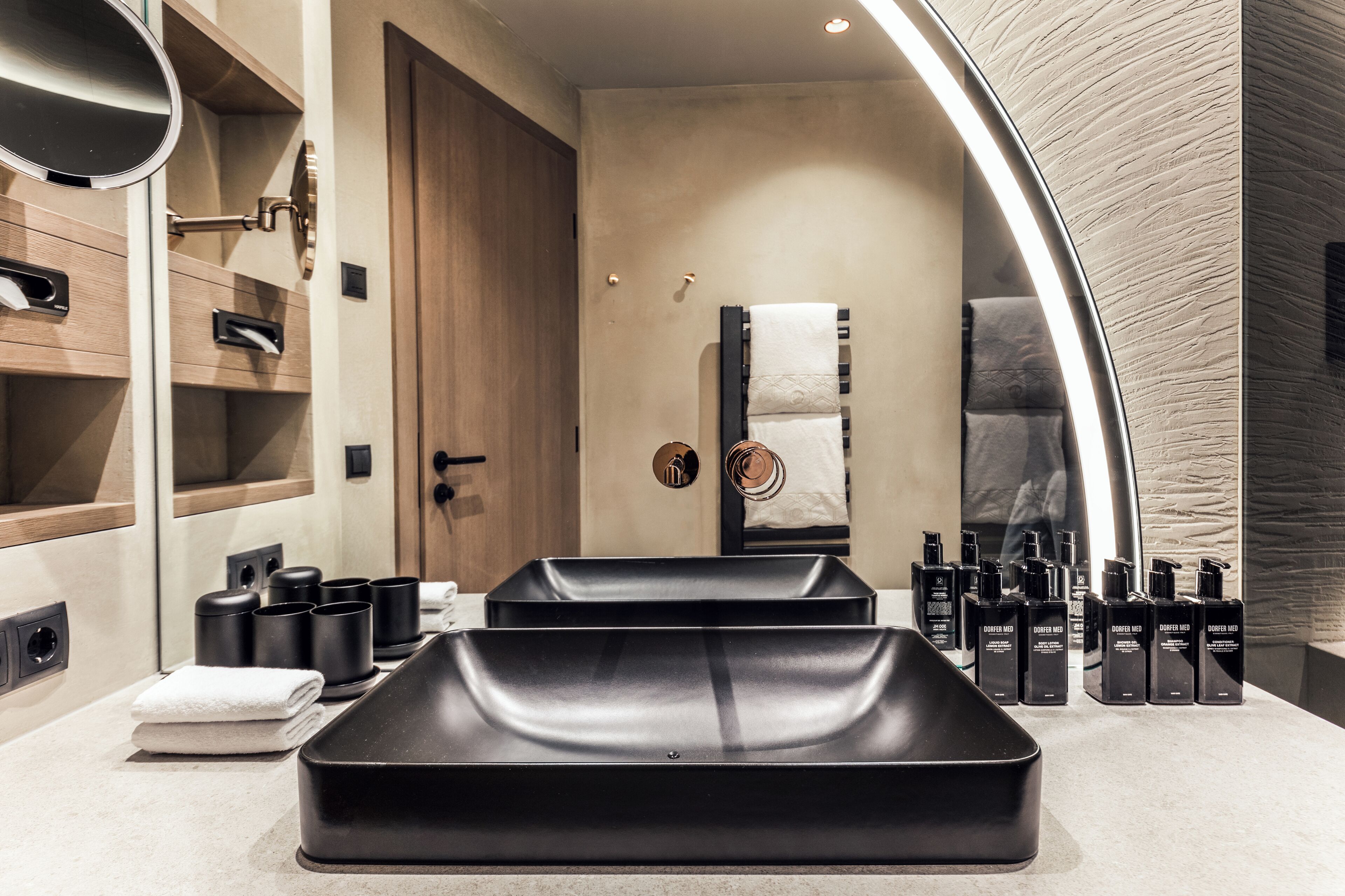 A modern bathroom with a large mirror, black sink, and neatly arranged toiletries.