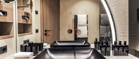 A modern bathroom with a large mirror, black sink, and neatly arranged toiletries.