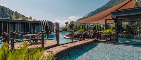 A pool area with wooden walkways, lounge chairs, and a view of mountains.