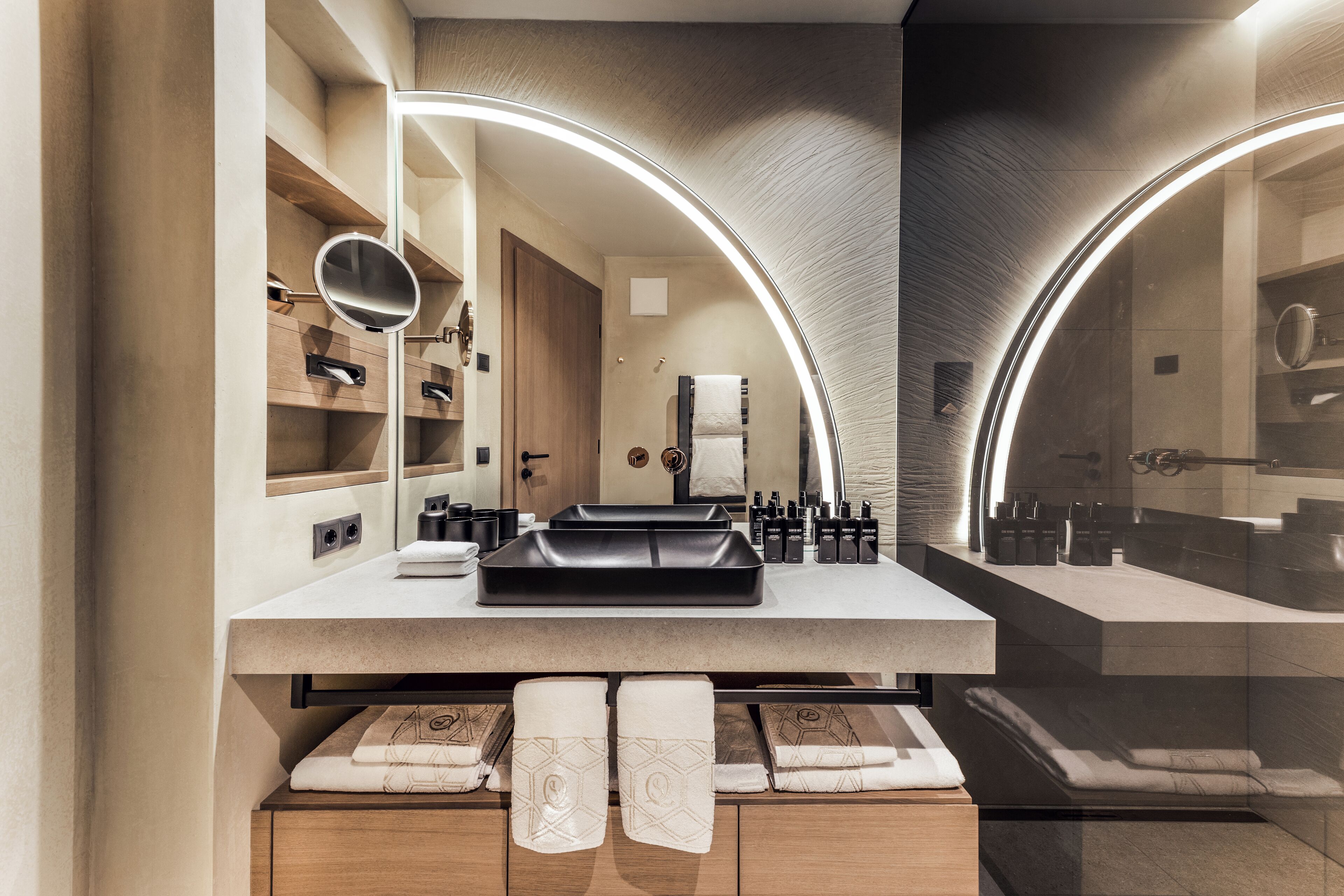 A modern bathroom with a large mirror, built-in shelves, and a vanity with a black tray.