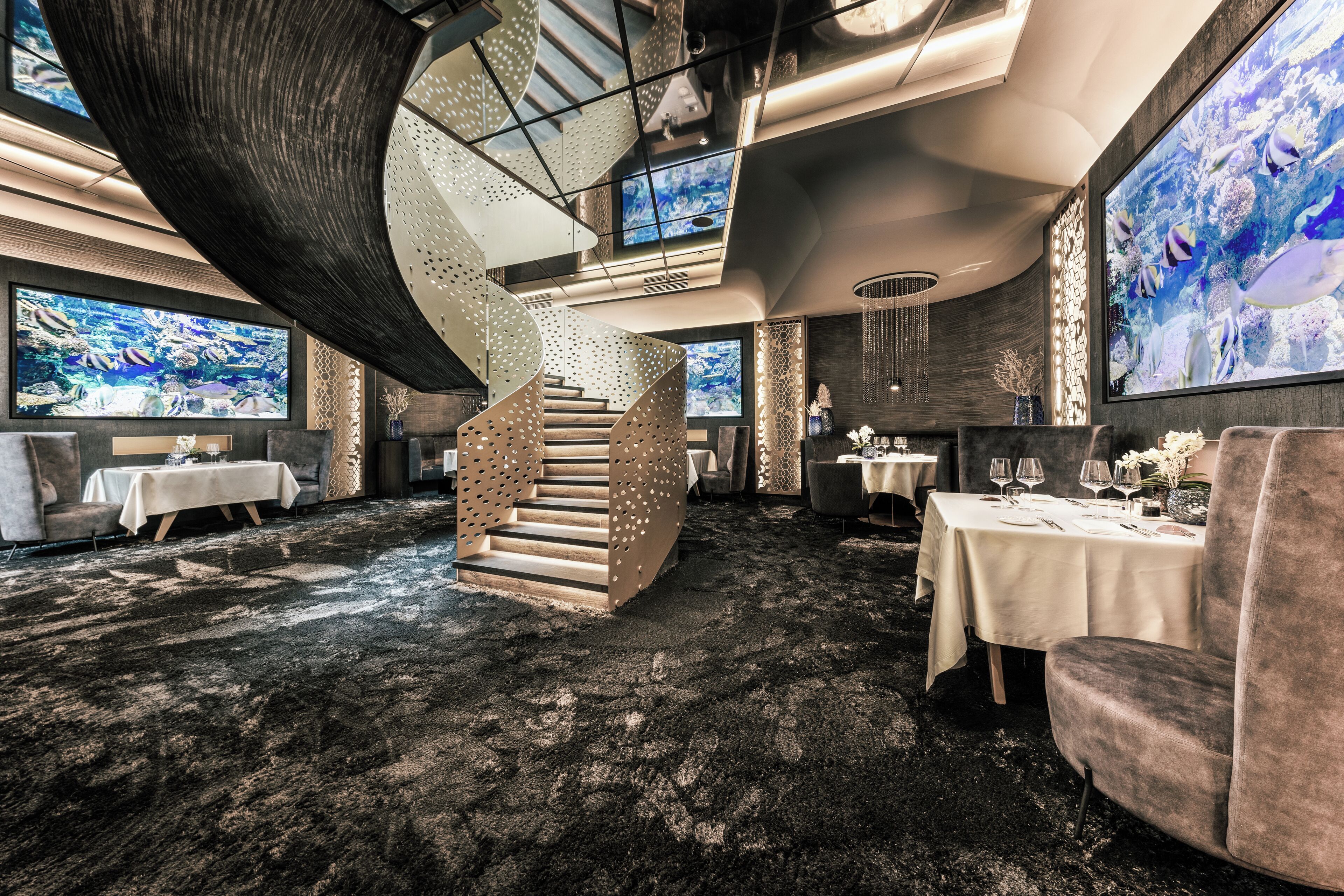 Un interior moderno con una escalera de caracol, varias mesas de comedor y grandes acuarios.