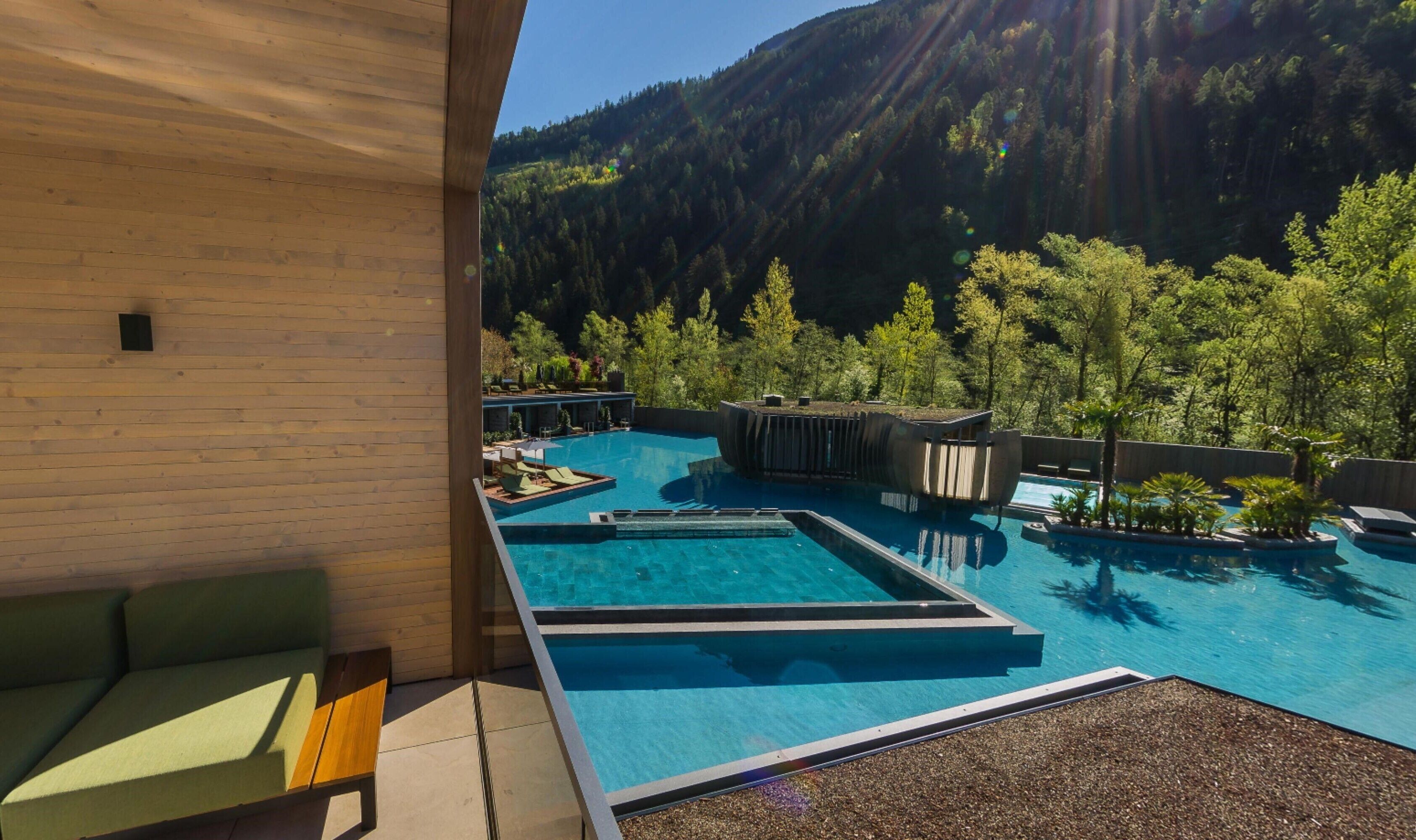 Un espace piscine comprenant plusieurs piscines, des chaises longues et une vue sur une montagne boisée.