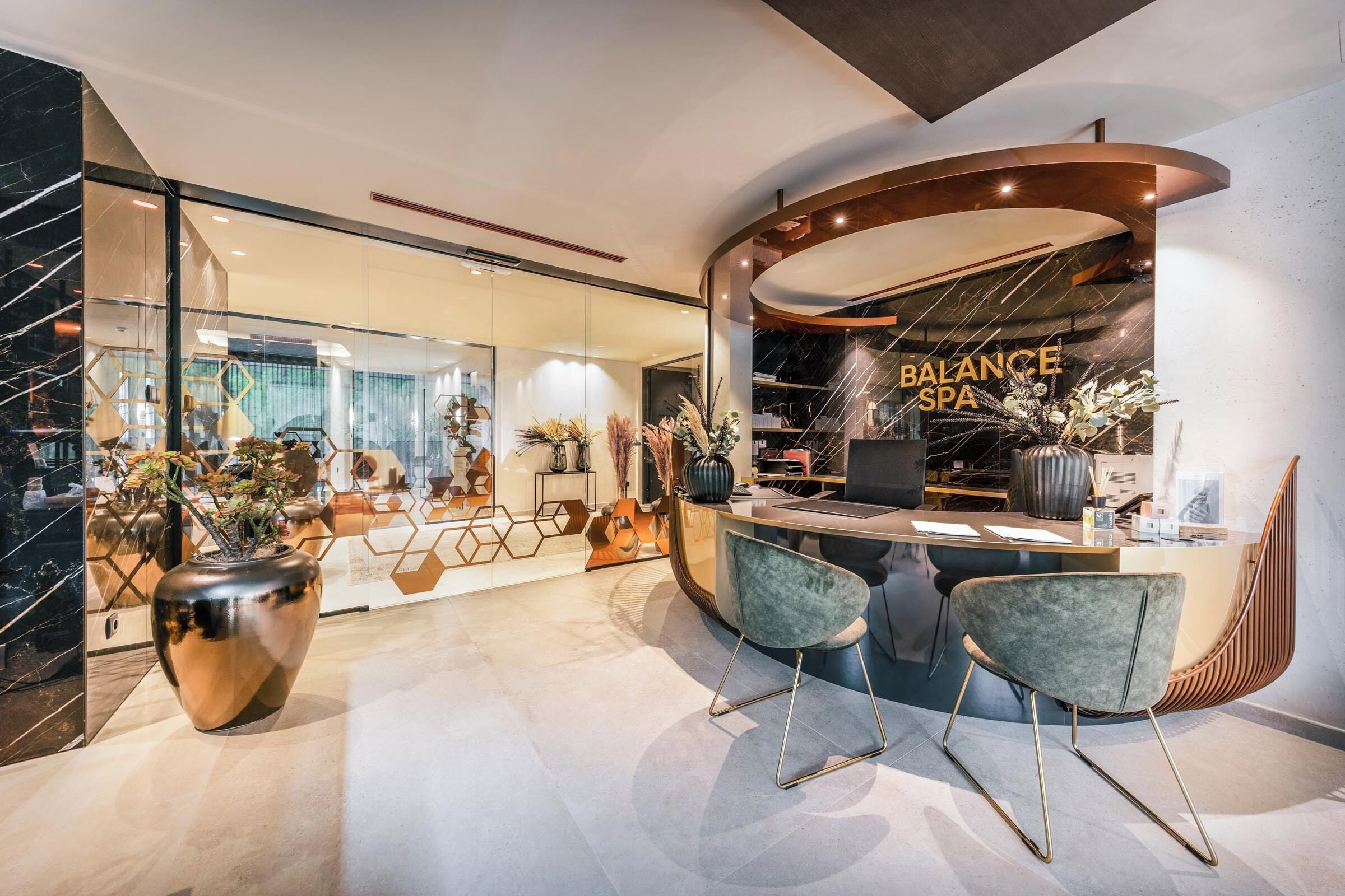 Ein modernes Spa-Interieur mit einer Rezeption, zwei Stühlen und einer großen Vase mit Pflanzen.