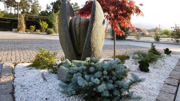 A garden with a unique rock sculpture, small shrubs, and a red-leaved tree. - Hotel A Queimada (A Estrada)