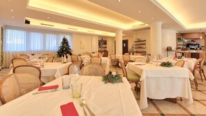 A dining area with tables set for a meal, a Christmas tree, and a kitchen area visible in the background. - Albergo Villa Priula (Sorisole)