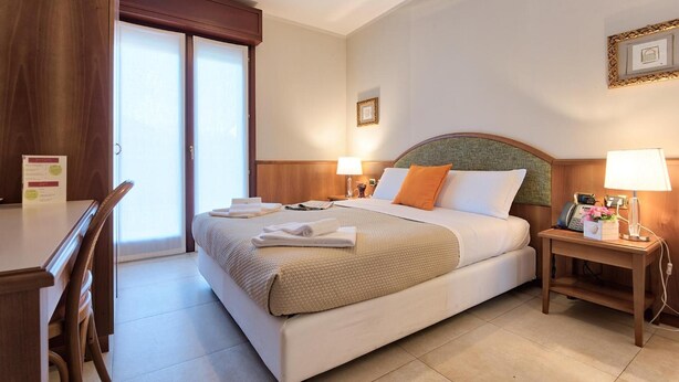 A hotel room with a large bed, two bedside tables with lamps, a wooden desk, and a chair. - Albergo Villa Priula (Sorisole)