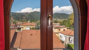 A view through a wooden-framed window with a brass handle, overlooking a town with terracotta-roofed buildings and green hills in the distance. - Albergo Villa Priula (Sorisole)