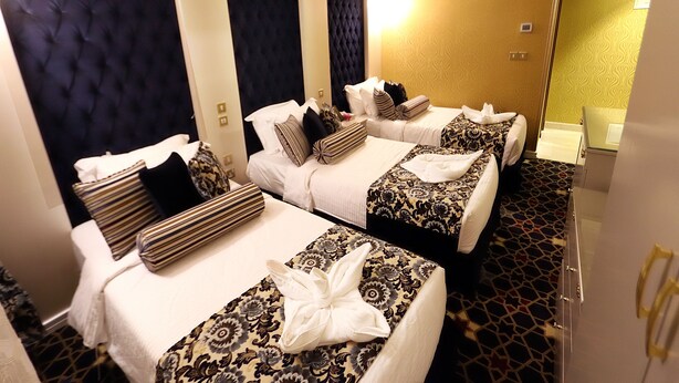 Ein Hotelzimmer mit zwei Betten, jeweils mit gemusterten Bettdecken und Kissen, einem dunklen Kopfteil und einem teppichartigen Bodenbelag.