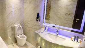 Ein modernes Badezimmer mit Marmorboden, einer weißen Toilette, einem Waschbecken mit Ablagefläche und einem großen Spiegel mit integrierter Beleuchtung.