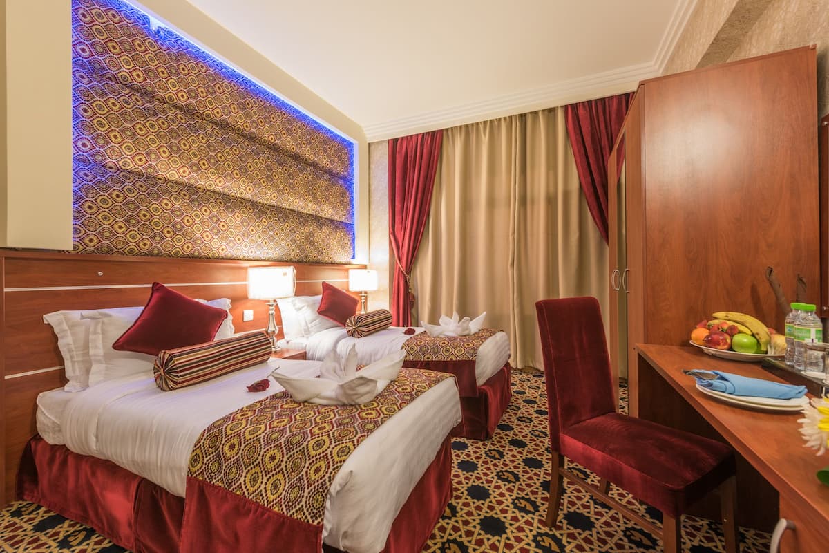 Ein Hotelzimmer mit zwei Betten, einem Holzschrank, einem Esstisch mit Obst und einer Wand mit Muster.