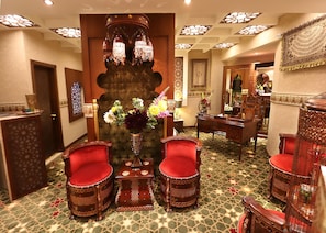 A luxurious lobby with ornate furniture, a central decorative column, and a patterned carpet.