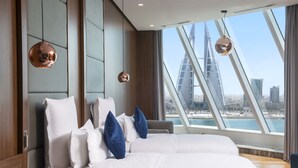 A modern hotel room with a large bed, a view of a city skyline, and a unique architectural feature in the background. - Wyndham Grand Manama (Manama)