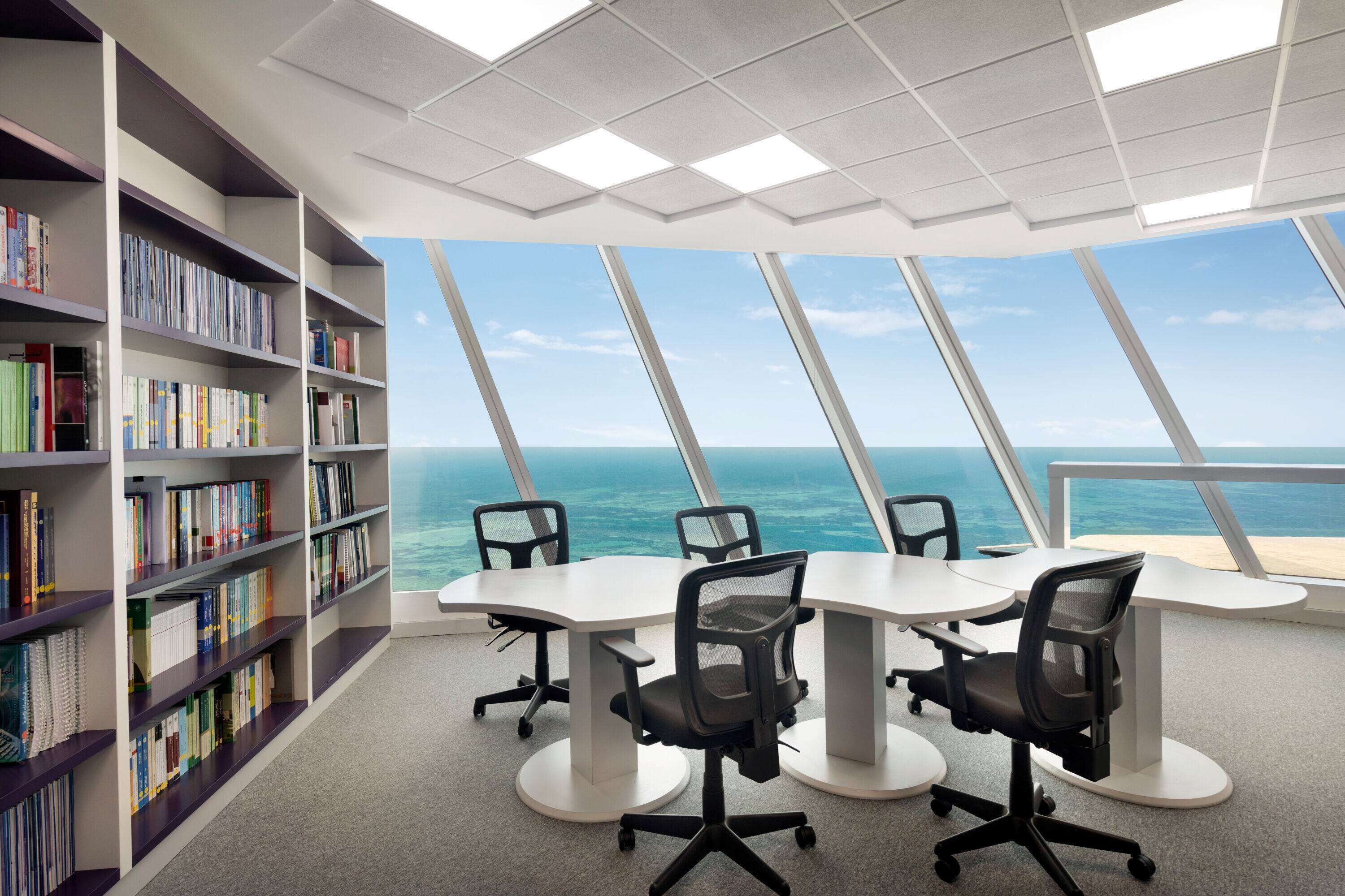 Una sala de conferències moderna amb una vista panoràmica a l'oceà, taules blanques, cadires d'oficina negres i una prestatgeria plena de llibres.