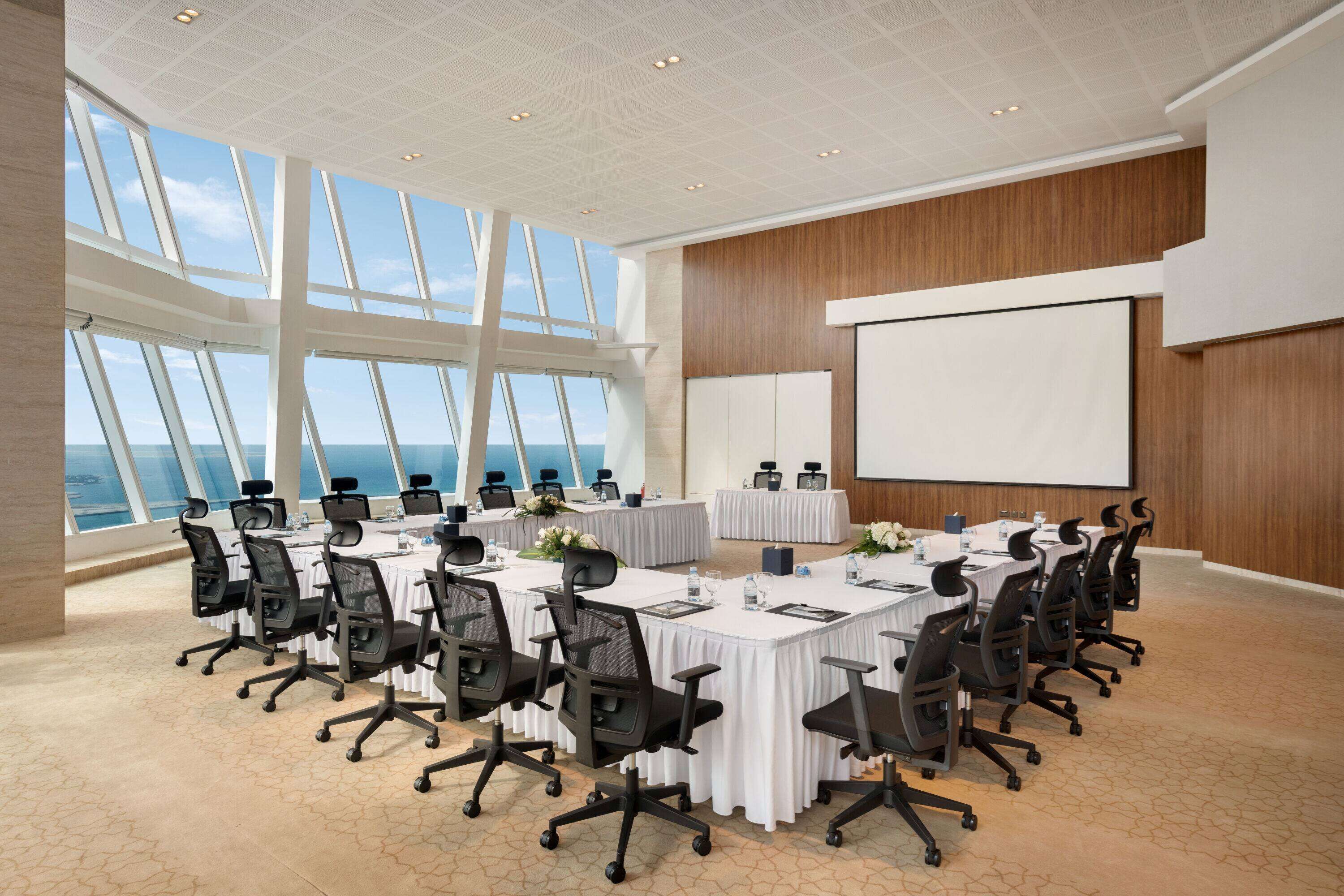 Une salle de conférence équipée d’une grande table, de chaises, d’un écran de projection et offrant une vue sur l’océan grâce à de grandes fenêtres.