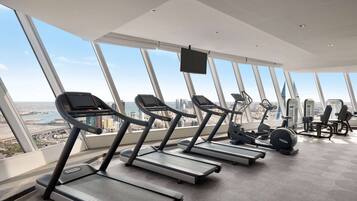 A gym with treadmills and exercise equipment, large windows with a city view.