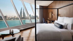 A modern hotel room with a large bed, a small table, and a chair. The room has a view of a city skyline and a body of water. - Wyndham Grand Manama (Manama)