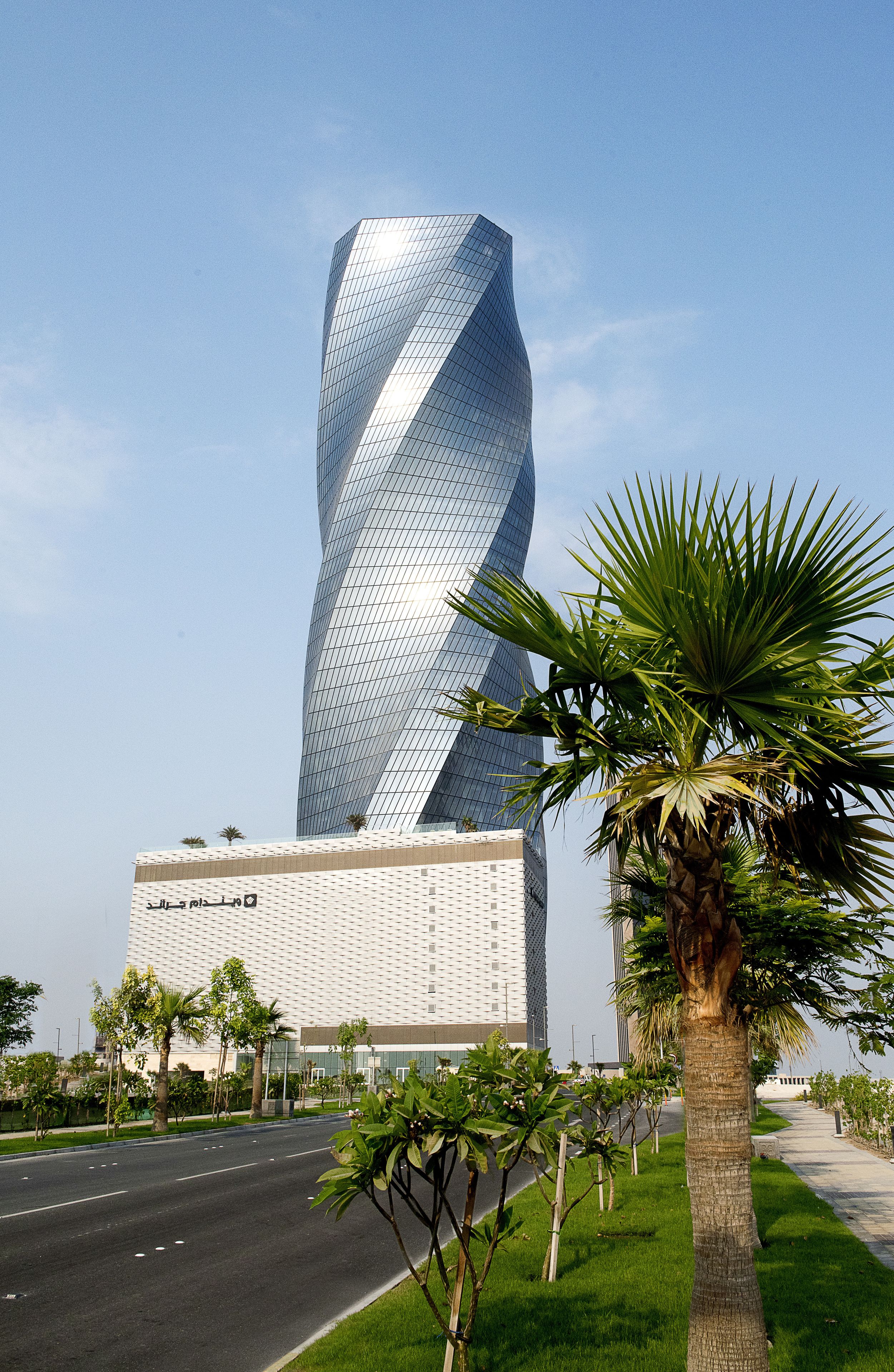 A modern building with a unique twisted design, surrounded by a well-maintained green space and a clear sky.