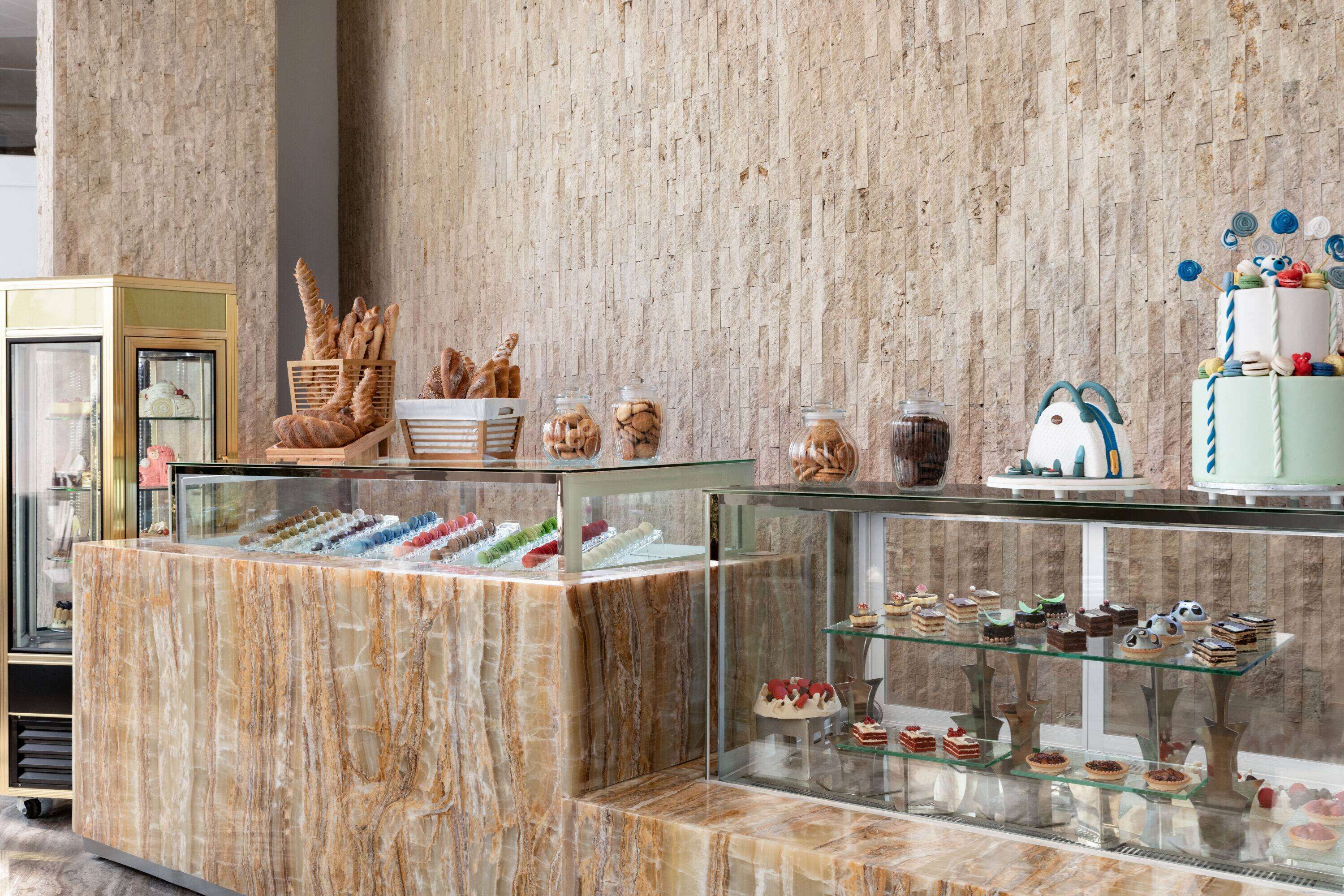 Mostrador de pastelería con diversos pasteles y tartas en una vitrina, frente a una pared con textura.