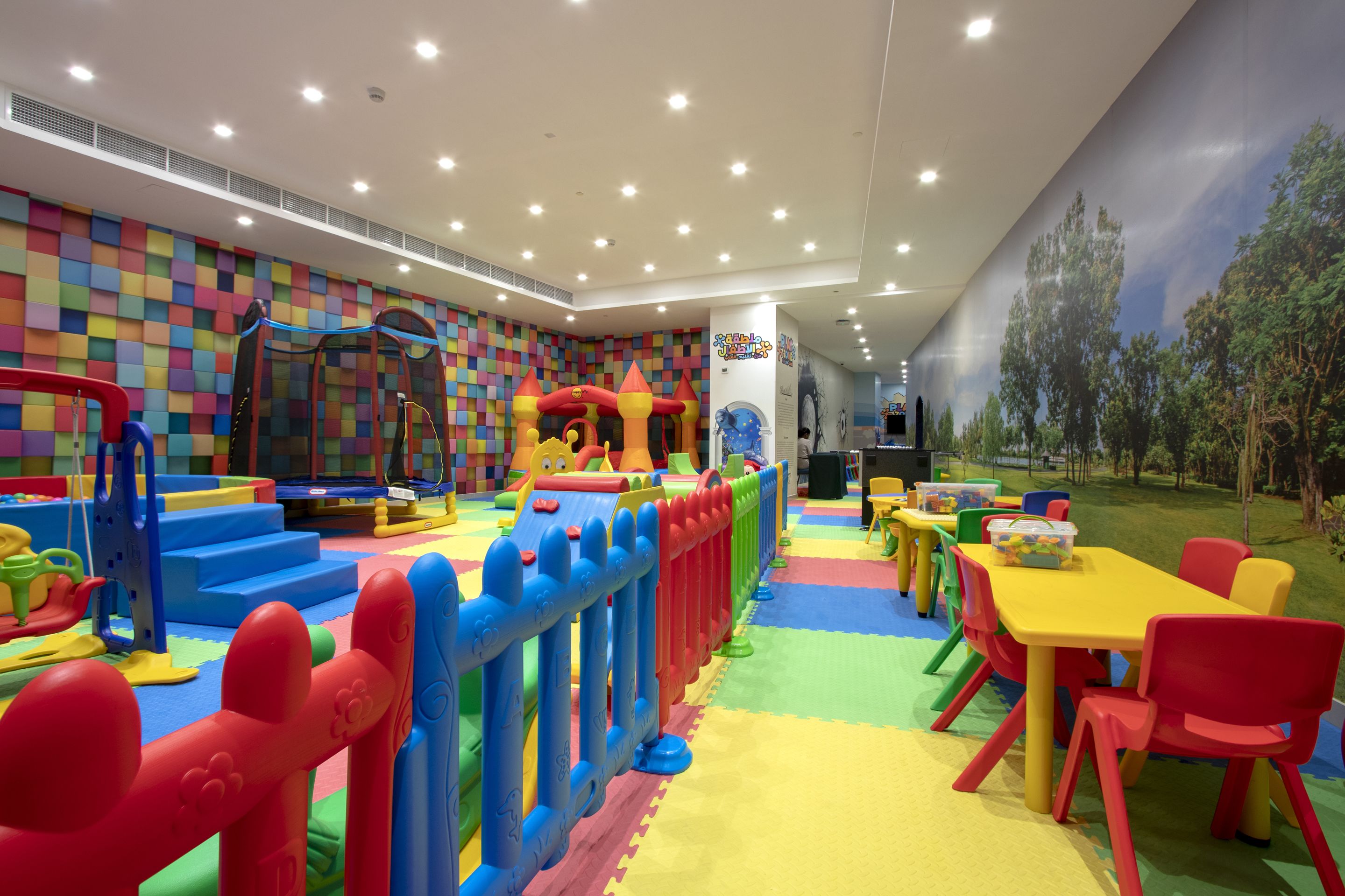 Zona de juegos infantiles con estructuras coloridas y un mural de árboles.