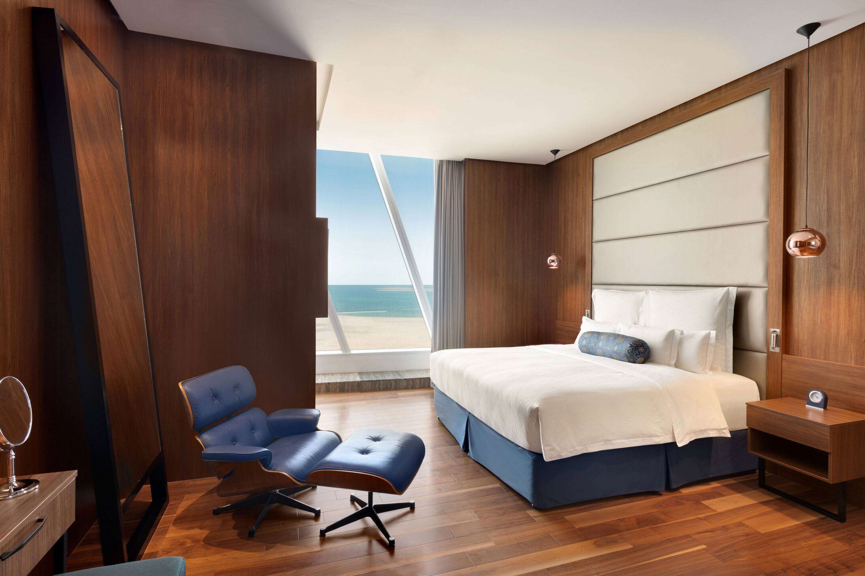 Una camera d'hotel moderna con un grande letto, una scrivania, una sedia e vista sul mare.