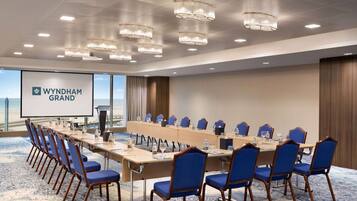 Un salón de conferencias con una mesa larga, sillas azules y una pantalla mostrando 'WYNDHAM GRAND'.