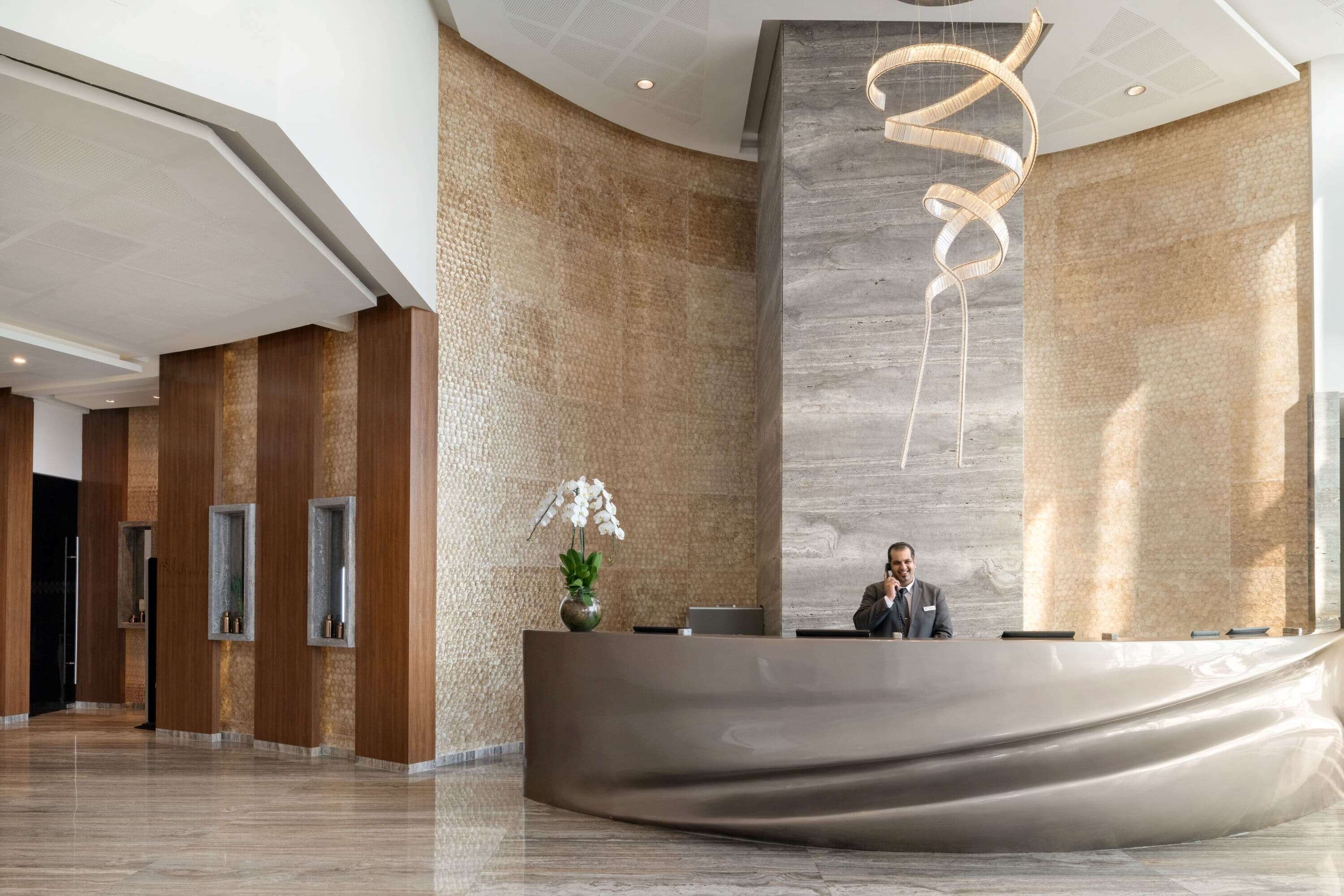 Un área de recepción moderna con un mostrador curvo, una recepcionista y una gran escultura abstracta.