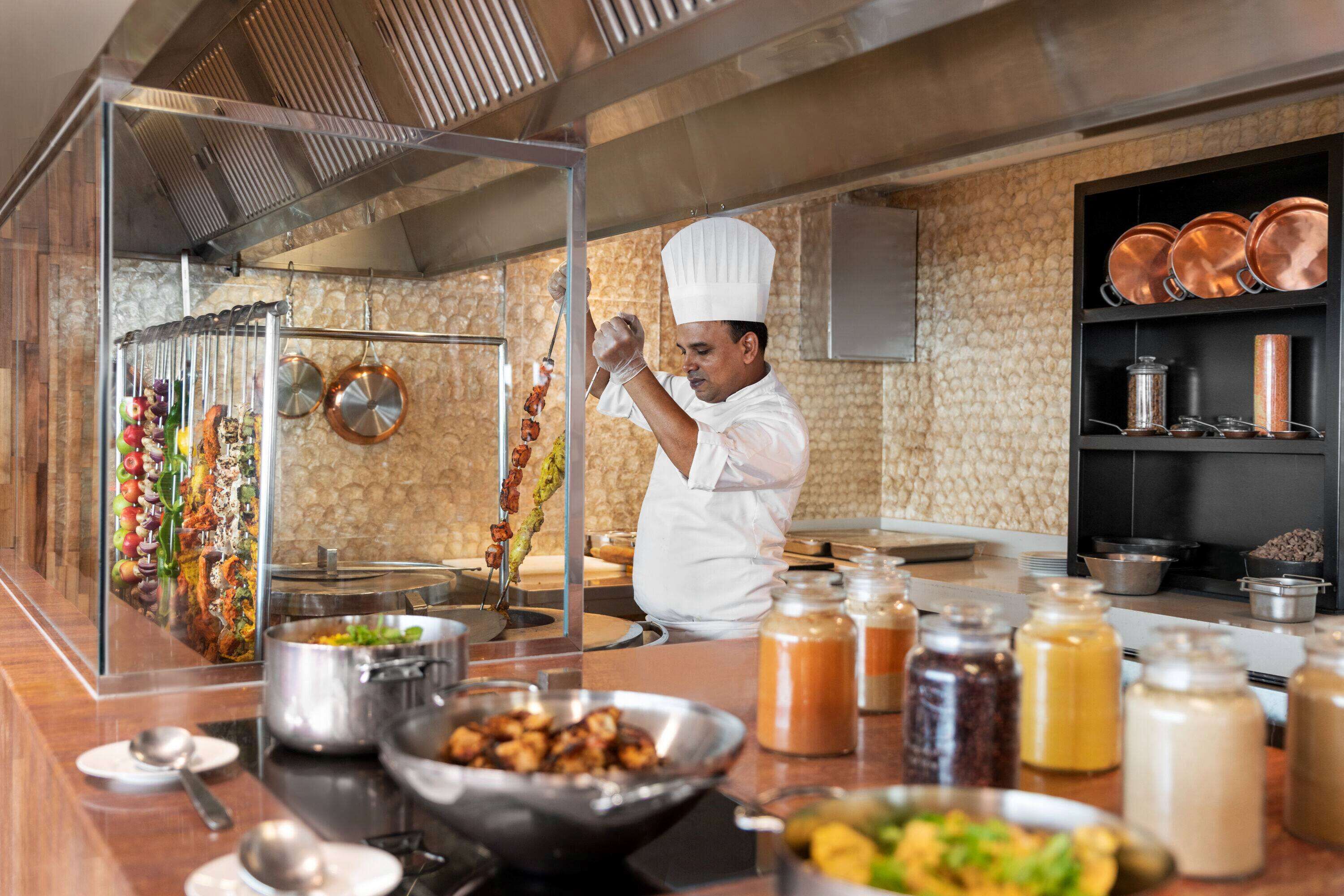 A chef preparing food in a kitchen with various cooking utensils, pots, and a display of vegetables.