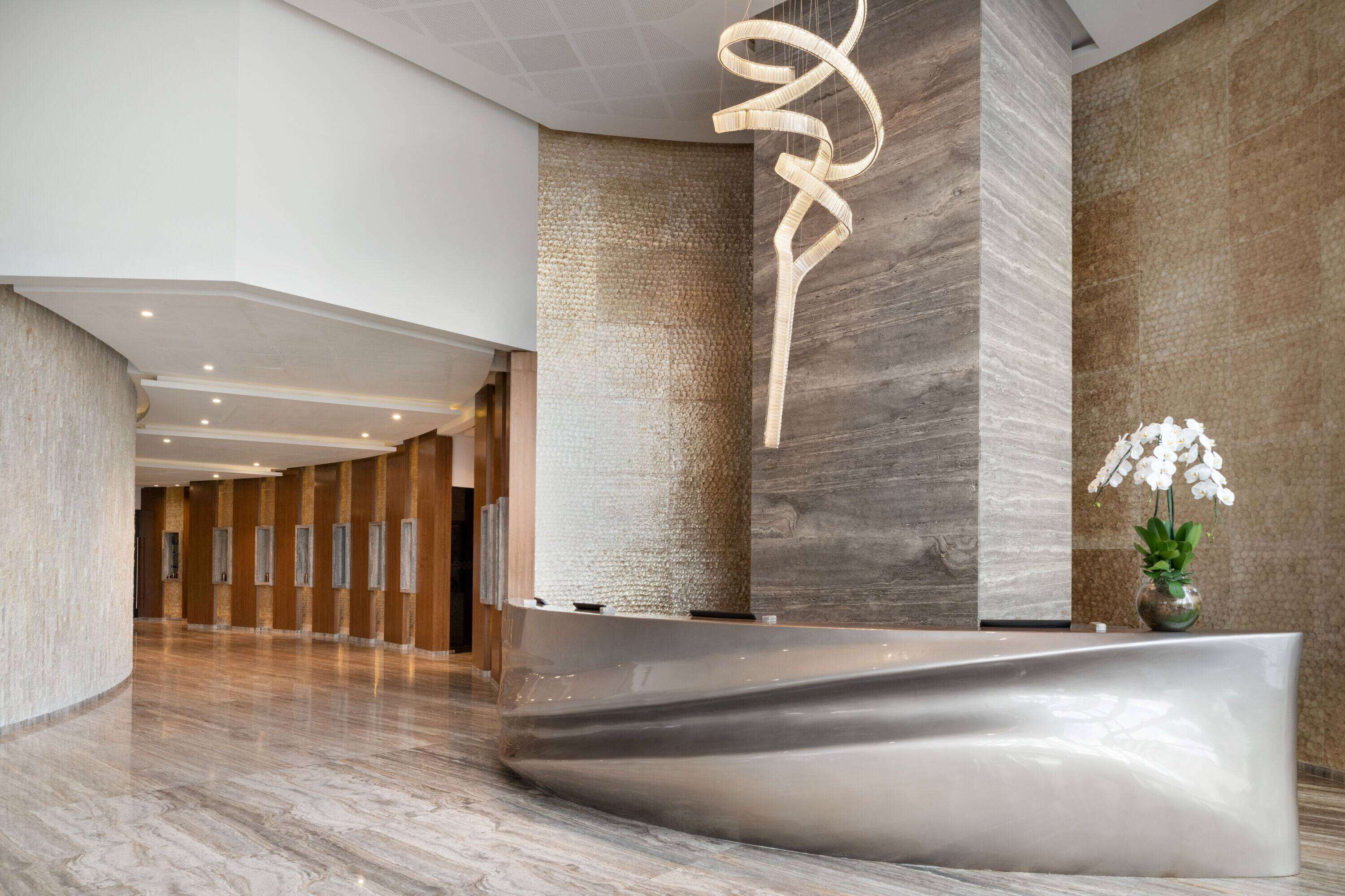 Una zona de recepción moderna con un mostrador curvo, una pared con textura y una lámpara colgante.