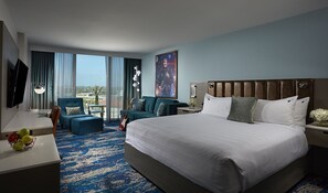 A hotel room with a large bed, two armchairs, a desk with a TV, and a view of the city. - Hard Rock Hotel Daytona Beach (Daytona Beach)