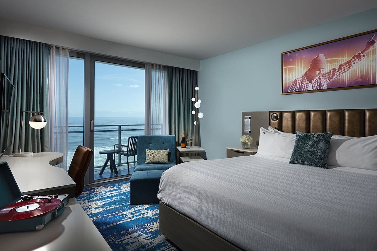 A hotel room with a large bed, a desk, a chair, and a view of the ocean.