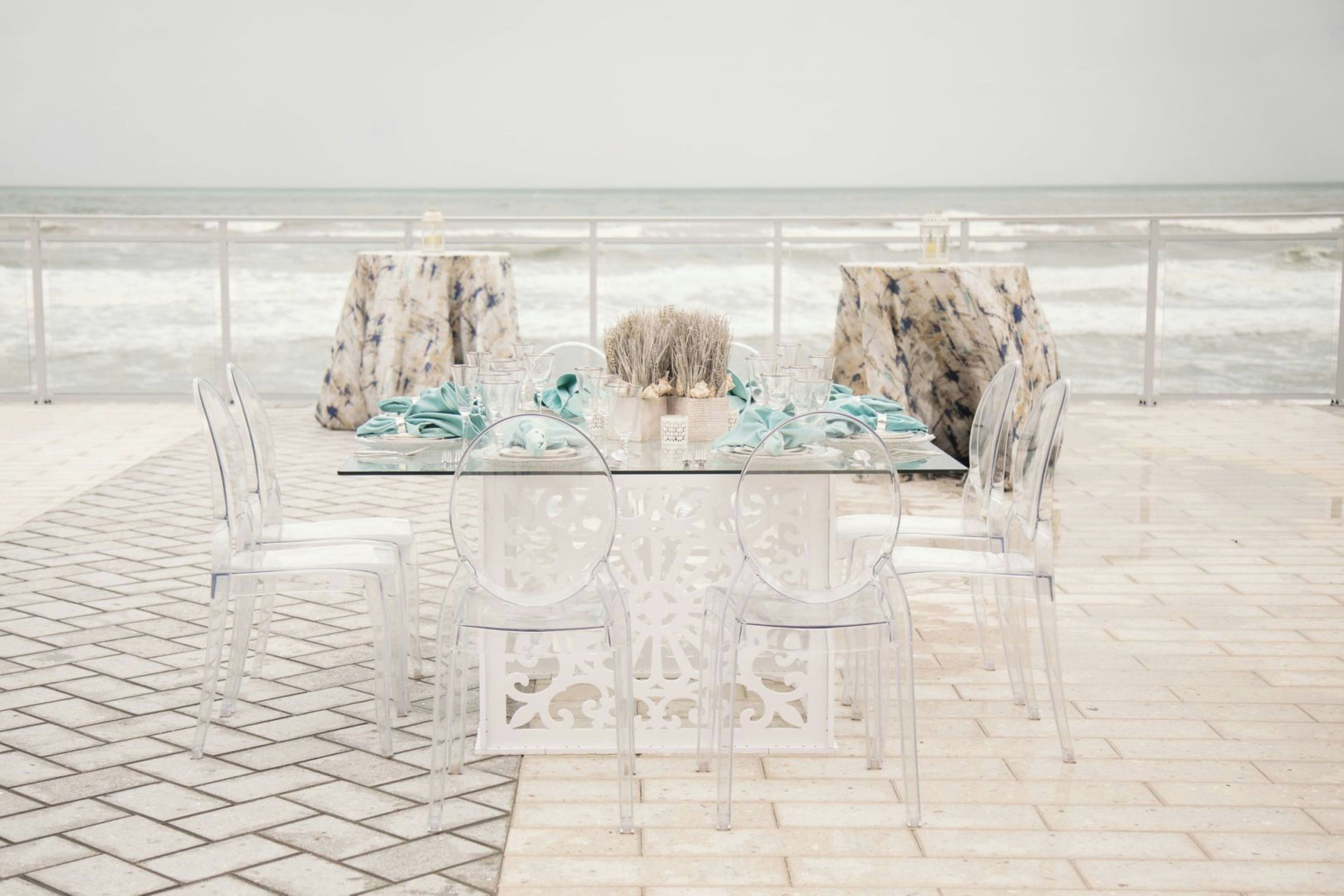 A table set for two with clear chairs, a marble table, and a view of the ocean.