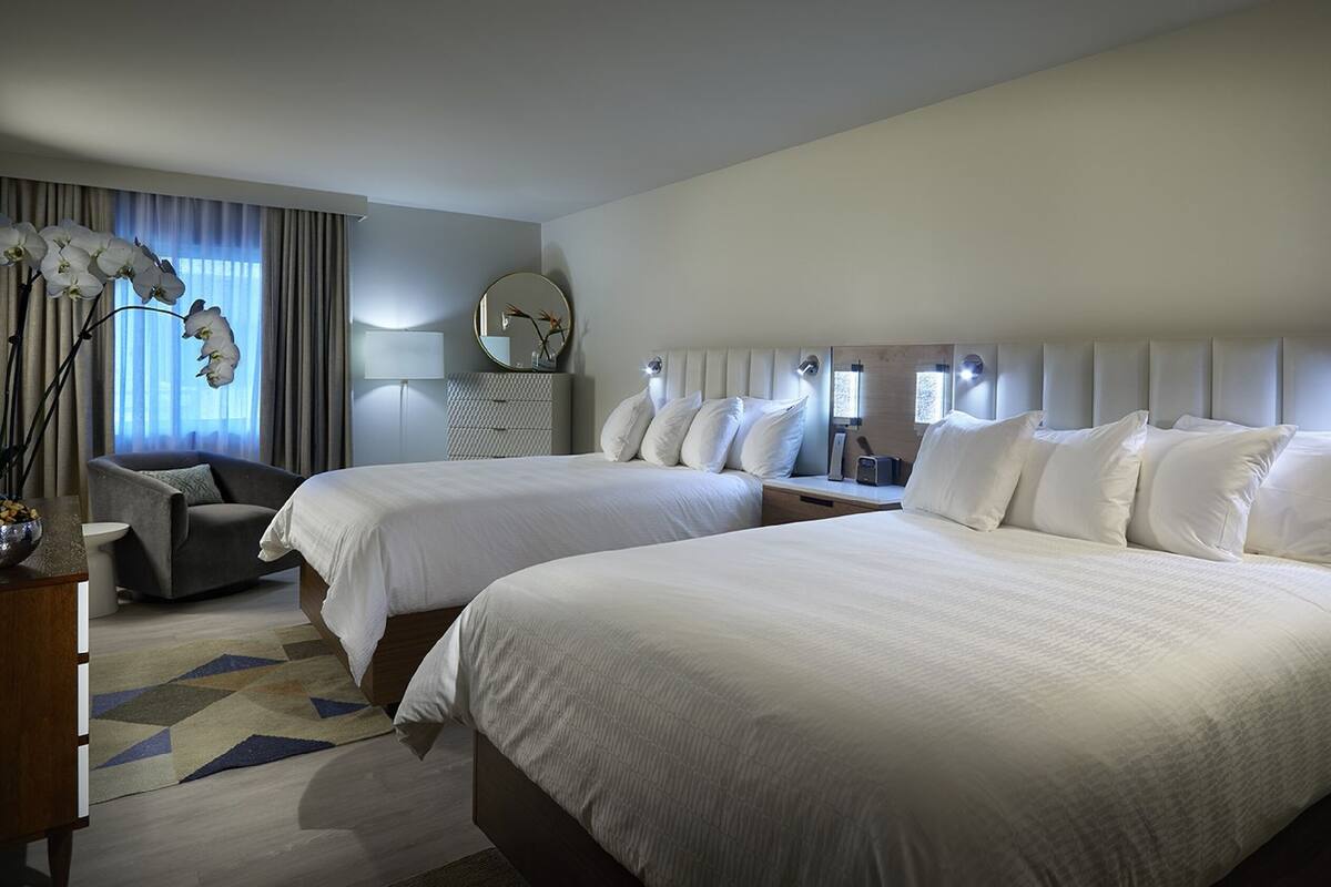 A hotel room with two beds, a desk, a chair, a lamp, and a window with curtains.