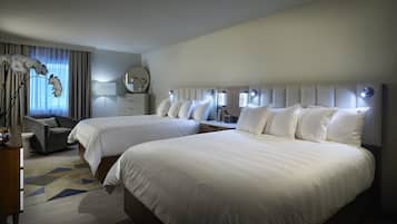 Una habitación de hotel con dos camas, un escritorio, una silla, una lámpara y un ventanal con cortinas.