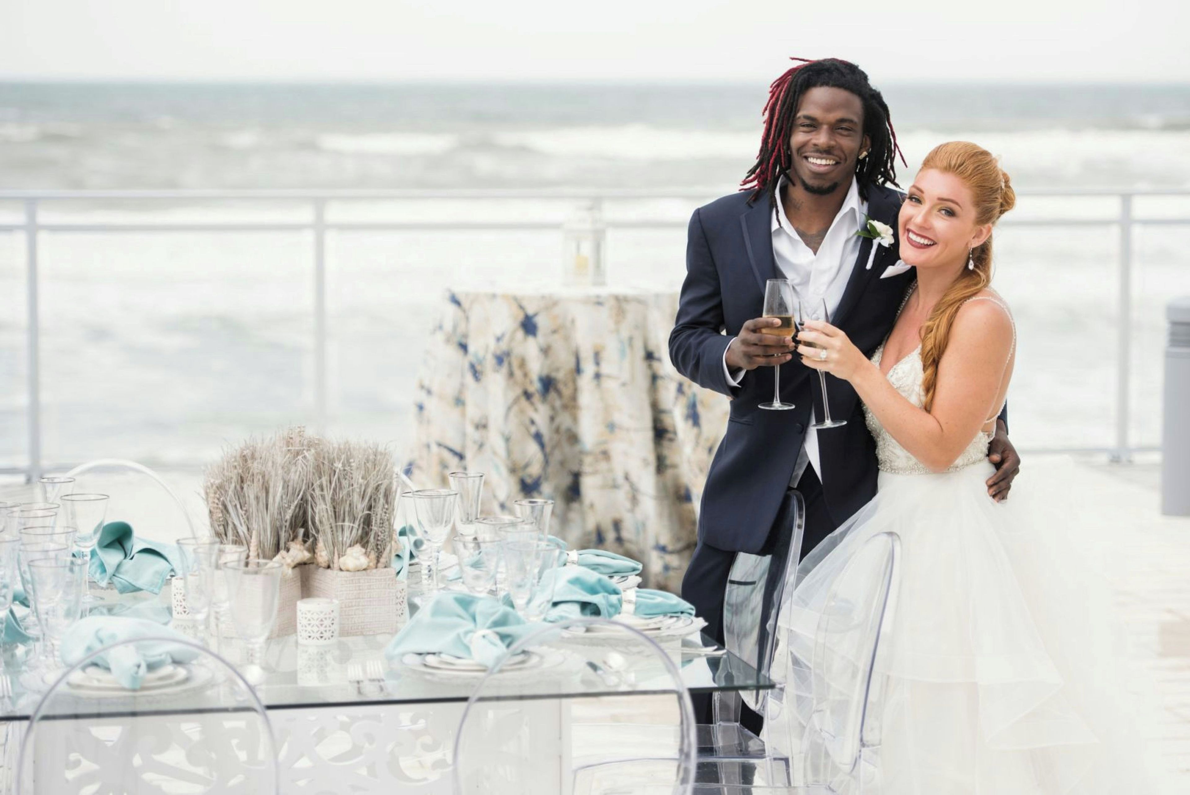 A couple at a table with a view of the ocean, holding wine glasses.